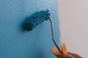 Close-up of male decorator painting wall in blue color. Man painting walls with roller. Repair and renovation of apartments concept
