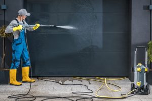 Caucasian Men in His 40s Powerful Pressure Washing Residential Garage Doors. Using Pressurized Water Jet to Clean Heavy Dirt.